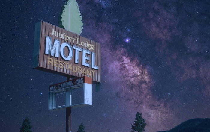 The milky way rises across a star filled sky behind the road sign for the abandoned Juniper Lodge Motel in California